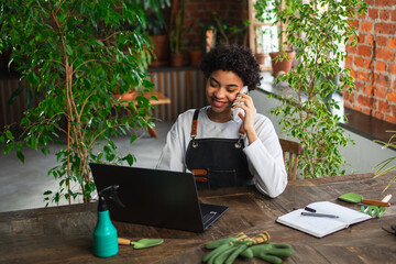 African woman florist gardener working in botanical store using laptop order plants by phone...