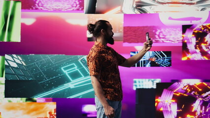 Young male performer feeling carefree with selfies and videos of himself, taking pictures on his mobile phone under cyberpunk visual art. Fun person enjoys a nightlife vibe. Camera B.