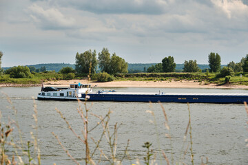 Cargo ship Natasja sailing downstream on the Rhine with green riverbank and sandy beach
