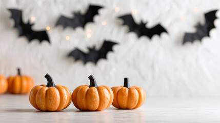 Halloween pumpkins on a white wooden table with bats on a white brick wall in the background