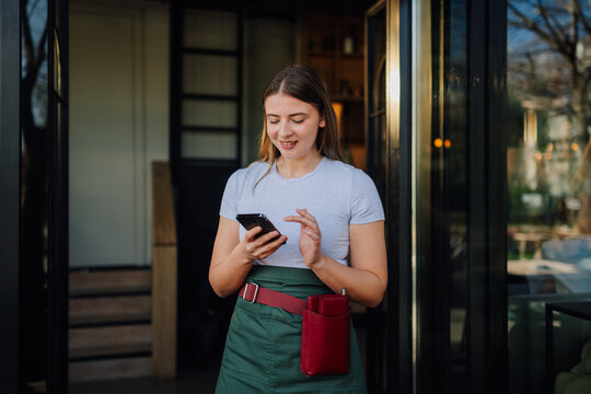 Waitress using smartphone at restaurant entrance, managing reservations and customer service