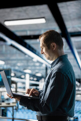 Engineer in data center managing software updates for system stability using laptop. Employee in...