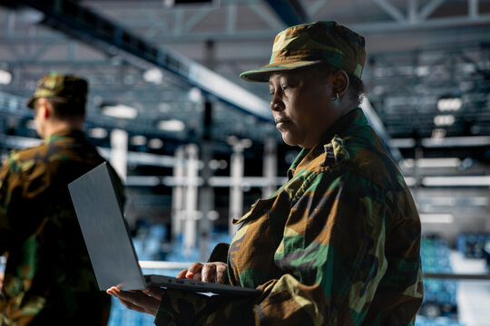 Female army IT specialist in data center using laptop to defend networks against cyber threats. Military command center admin using notebook to identify potential intrusions or malicious activities