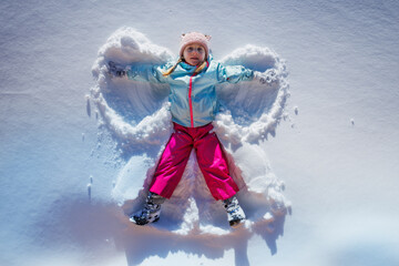 Happy girl create snow angels, lying happily in winter clothing