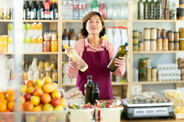 Experienced female salesperson offers choice of buying bottle of vegetable oil or olive oil in a grocery store