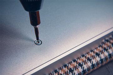 A close-up view of a screwdriver inserting a screw into a metallic surface, showcasing precision work.