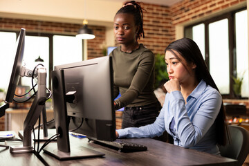 Asian female editor sitting and reviewing product designs on computer, as black woman manager...