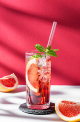 Refreshing cocktail with grapefruit, mint and ice in a glass on a white red background with shadow