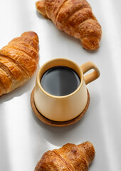 Coffee espresso in yellow cup and fresh croissants on white background with morning shadows.