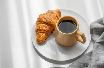 Coffee espresso in yellow cup and fresh croissant on a plate on white background