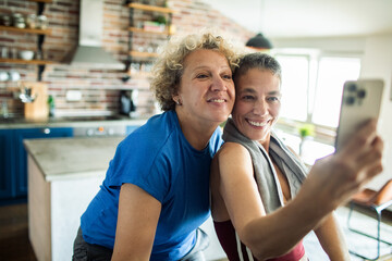 Happy mature lesbian couple taking a selfie together after home workout