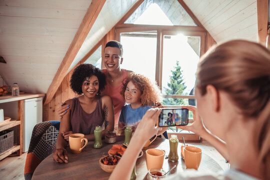 Young and diverse group of female friends having breakfast and taking a photo with a smart phone together in a cabin in the forest