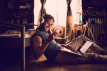 Young man using a smart phone and laptop whie listening to music in the bedroom