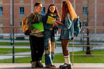 Three multiracial university students chatting together on campus after class, holding notebooks...