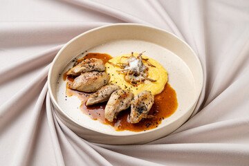 A beautifully arranged dish showcases tender meat paired with creamy polenta and a rich sauce, garnished with crispy toppings. This exquisite culinary delight is perfect for fine dining