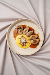 This culinary masterpiece features a smooth serving of polenta, elegantly garnished with delicious dumplings drizzled in a rich sauce, all artfully presented on soft fabric
