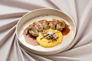 A beautifully plated dish showcases tender meat drizzled with rich sauce, accompanied by creamy polenta and topped with crispy onions. Perfectly presented for a fine dining experience