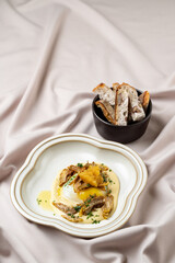 A beautifully arranged plate showcases tender artichokes drizzled with sauce, accompanied by crispy bread, set against a soft fabric backdrop, inviting a warm dining atmosphere