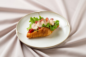 Savor the exquisite flavor of a buttery croissant filled with succulent lobster meat, crisp lettuce, and juicy tomatoes, beautifully presented on a soft fabric backdrop