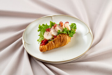A delicious croissant, carefully filled with succulent seafood, nestled on a simple white plate....
