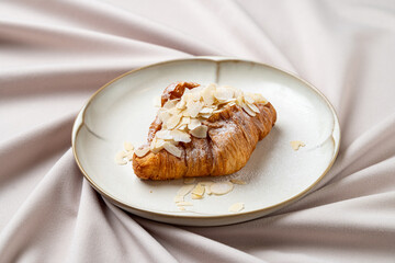 A beautifully baked almond croissant adorned with thinly sliced almonds rests on a simple ceramic plate