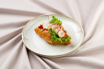 A delightful croissant sits elegantly on a plate, adorned with fresh lobster and vibrant lettuce. The warm hues and soft textures create a cozy atmosphere perfect for a gourmet experience