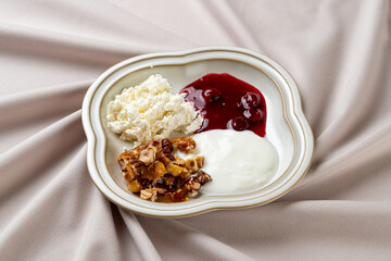 A beautifully arranged dessert platter showcases creamy cheese, vibrant berry sauce, and crunchy nut mix, elegantly set on a soft, lush tablecloth. A perfect indulgence for any occasion