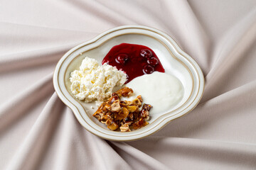 A beautifully arranged plate showcases a harmonious blend of creamy yogurt, a vibrant cherry topping, and crunchy nut granola, all set on a soft, neutral fabric backdrop