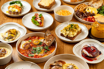 A delightful assortment of brunch dishes is beautifully arranged on a wooden table. Plates feature...