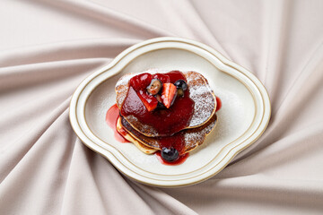 Fluffy heart-shaped pancakes topped with a rich berry sauce and fresh fruits, resting elegantly on a delicate plate, evoke feelings of love and indulgence during a cozy morning