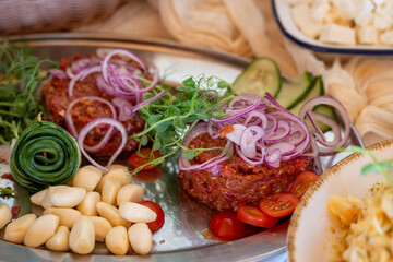 Minced meat tartare arranged on a metal tray with garlic, tomatoes, and onions for buffet guests. 
