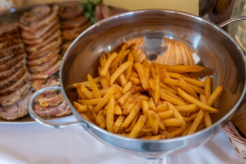 A metal bowl filled with crispy fried French fries on the buffet table for guests. 
