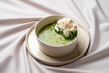 A vibrant green soup sits elegantly in a smooth bowl, adorned with succulent crab meat, capturing the essence of coastal flavors and fresh ingredients. Perfect for a warm meal