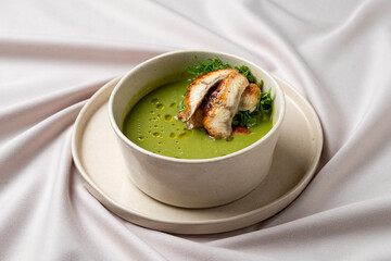 A hearty bowl of vibrant green soup, featuring tender pieces of grilled chicken on top, garnished with fresh herbs, sits elegantly on a textured plate, perfect for a gourmet meal