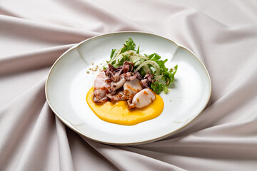A beautifully arranged dish showcases tender seafood alongside fresh greens, drizzled with a vibrant sauce, all set on a delicate tablecloth in a fine dining atmosphere