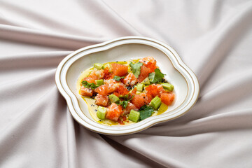 Diced salmon and avocado are beautifully arranged in a stylish bowl, garnished with fresh herbs, set against a draped linen backdrop that enhances the vibrant colors of the dish