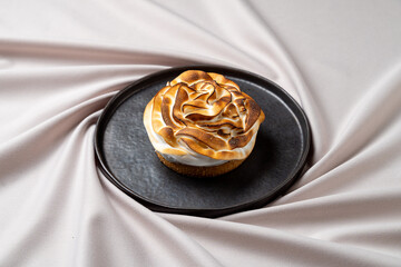 A delightful rose-shaped dessert sits atop a sleek black plate, showcasing intricate details and a perfectly toasted exterior. The soft, creamy texture invites indulgence