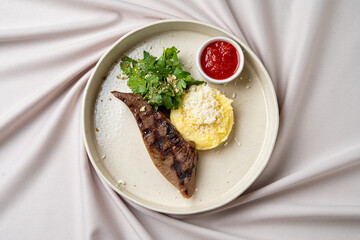 A beautifully arranged plate features juicy grilled steak alongside smooth mashed potatoes topped with herbs and cheese