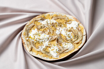A delectable treat showcases a blend of creamy layers topped with crunchy nuts, elegantly presented on a soft, draped fabric. This culinary delight invites indulgence and satisfaction
