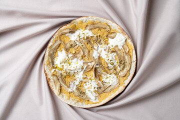A warm flatbread is adorned with smooth yogurt and tender grilled chicken slices, sprinkled with crushed pistachios, creating an inviting feast. The neutral fabric enhances the dish's vibrant colors