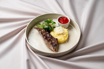 Savor the delightful combination of grilled fish accompanied by creamy mashed potatoes, fresh herbs, and a side of tangy sauce on a beautifully draped surface
