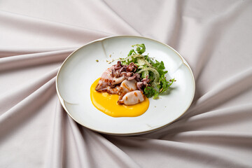 Delicate grilled octopus is artistically arranged on a crisp white plate, accompanied by a creamy sauce and fresh greens. Soft fabrics drape underneath, enhancing the gourmet presentation