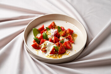 Juicy watermelon chunks are artfully arranged with dollops of creamy topping, herbs, and a sprinkle of crunchy elements, creating a harmonious dish showcasing vibrant flavors