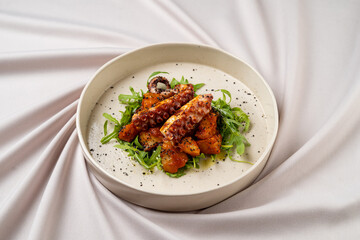 Delight in a plate of beautifully roasted octopus, accompanied by peppery greens, served on a smooth canvas. The delicate balance of flavors invites exploration and appreciation