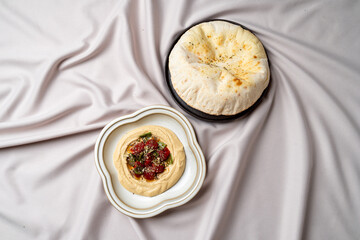 A delicious spread showcases a smooth and creamy hummus adorned with fresh vegetables, complemented by a warm, fluffy pita bread set against a stylish backdrop. Perfect for sharing