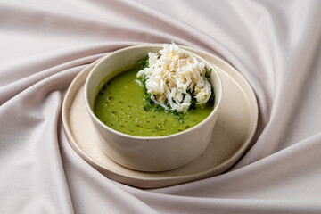 A comforting bowl features vibrant green soup enriched with herbs, topped with delicate crab meat. The setting is elegantly styled, presenting a cozy culinary moment