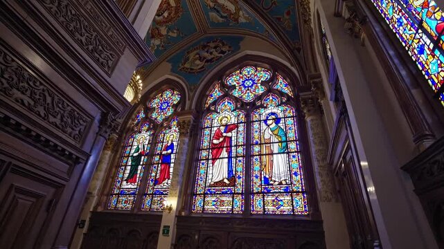 Wide-angle shot of an ornate church interior with stained glass windows and chandeliers, capturing a serene and majestic atmosphere for a video setting.
