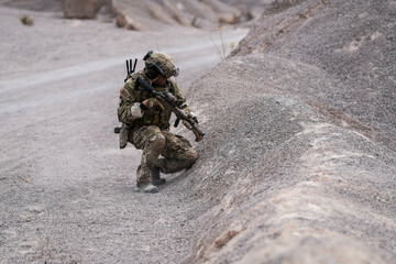 Modern Soldiers on Recon Mission – Two Armed Men in Military Camouflage Patrolling a Rocky Terrain During a Tactical Operation with Weapons Ready in a Desert-like Environment