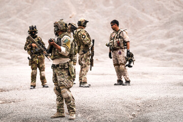 Special Forces Team Standing Together in Desert Mountain Terrain – Tactical Soldiers in Full Gear with Rifles, Communicating and Coordinating During a Military Operation or Training Mission