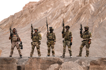 Special Forces Team Standing Together in Desert Mountain Terrain – Tactical Soldiers in Full Gear...